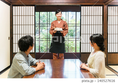 旅館,料亭で夫婦,カップルのいる客室に日本茶を運ぶ女性スタッフ,仲居,女将 旅館,料亭で夫婦,カップルのいる客室に日本茶を運ぶ女性スタッフ,仲居,女将 140527616