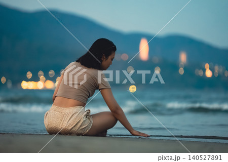 Woman sitting on shoreline beside sea waves during peaceful tropical evening by coast and playing with sand, Female traveler relaxing on sandy beach with ocean surf and calm seaside atmosphere Woman sitting on shoreline beside sea waves during peaceful tropical evening by coast and playing with sand, Female traveler relaxing on sandy beach with ocean surf and calm seaside atmosphere 140527891