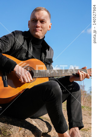 Blonde man playing string guitar outdoors in autumn forest. Concept of sound therapy, mental health and wellness rituals. Calmness tranquility audio-sensory practices. Aura farming energy Blonde man playing string guitar outdoors in autumn forest. Concept of sound therapy, mental health and wellness rituals. Calmness tranquility audio-sensory practices. Aura farming energy 140527984