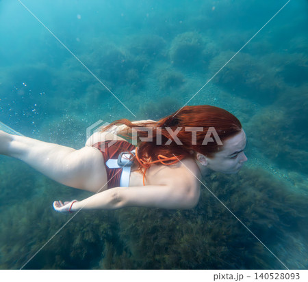 Freediving redhead underwater woman with long red hair dives through a clear blue sea above the ocean floor to explore marine life 140528093