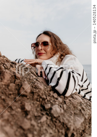 Woman sunglasses sweater leaning on a coastal rock while looking at the sea during a peaceful autumn day outdoors Woman sunglasses sweater leaning on a coastal rock while looking at the sea during a peaceful autumn day outdoors 140528134