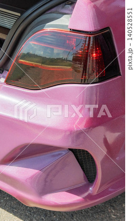 Vibrant pink custom painted car showcasing detailed rear light and bumper design, highlighting craftsmanship of tuning and personalization of vehicle, vertical photo format capturing unique automotive 140528551