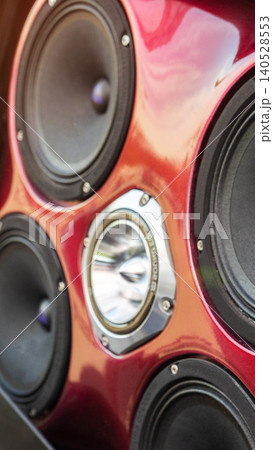 Close-up view of multiple car audio speakers with central reflective tweeter installed on custom glossy red panel, vertical photo capturing detail of sound system enhancement for vehicle tuning 140528553