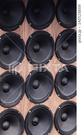 Black car audio speakers systematically mounted on textured wooden panel. Many powerful sound system components arranged in vertical rows, highlighting modern automotive acoustics design. 140528609
