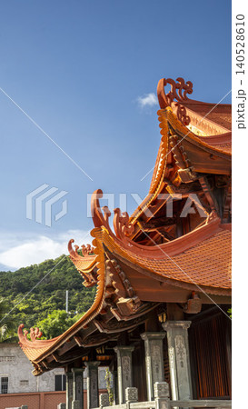 Detailed close-up of ornate curved eaves and intricate wood carvings of a traditional Vietnamese temple roof against a bright blue sky. Masterful craftsmanship. Detailed close-up of ornate curved eaves and intricate wood carvings of a traditional Vietnamese temple roof against a bright blue sky. Masterful craftsmanship. 140528610