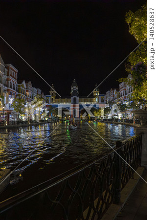 Night view down a glowing Venice-style canal toward an ornate illuminated arch bridge with gondola, colorful European buildings and festive lights in Phu Quoc, Vietnam. Night view down a glowing Venice-style canal toward an ornate illuminated arch bridge with gondola, colorful European buildings and festive lights in Phu Quoc, Vietnam. 140528637