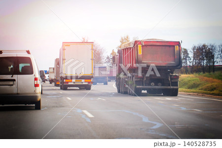 Rear view of trucks and van on highway under bright sky, transportation movement on open road, vehicle caravan driving into distant sun flare 140528735