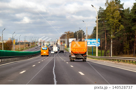 Multi-lane highway traffic view from behind orange garbage truck and orange bus, urban landscape backdrop, overcast sky, autumn day transportation scene 140528737