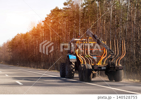 Heavy duty forestry forwarder machine moving on asphalt road, rear view, equipment for timber transportation, logging vehicle, forest backdrop Heavy duty forestry forwarder machine moving on asphalt road, rear view, equipment for timber transportation, logging vehicle, forest backdrop 140528755
