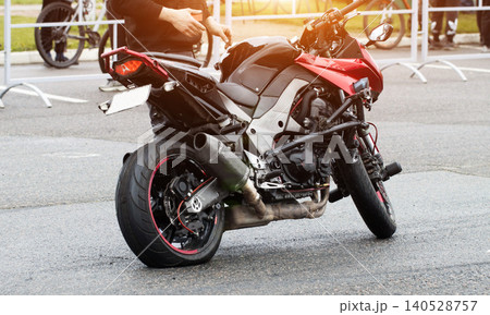 Sport motorcycle with flat rear tire on asphalt road. Person stands near damaged bike, preparing for repair or inspection of broken vehicle. Breakdown of high-performance two-wheeler. Sport motorcycle with flat rear tire on asphalt road. Person stands near damaged bike, preparing for repair or inspection of broken vehicle. Breakdown of high-performance two-wheeler. 140528757