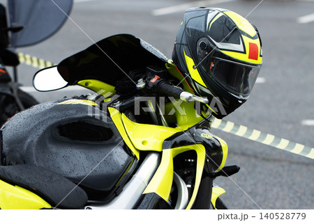 Motorcycle with vibrant neon yellow and black racing helmet parked outdoors on wet asphalt surface showing water droplets after rain Motorcycle with vibrant neon yellow and black racing helmet parked outdoors on wet asphalt surface showing water droplets after rain 140528779