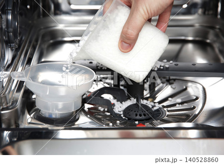 Hand pouring dishwasher salt crystals into funnel of dishwasher water softener compartment for appliance maintenance and optimal performance Hand pouring dishwasher salt crystals into funnel of dishwasher water softener compartment for appliance maintenance and optimal performance 140528860