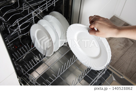 Person hand placing clean white dish into modern dishwasher appliance, kitchen chore completion, household efficiency device for clean dishes Person hand placing clean white dish into modern dishwasher appliance, kitchen chore completion, household efficiency device for clean dishes 140528862