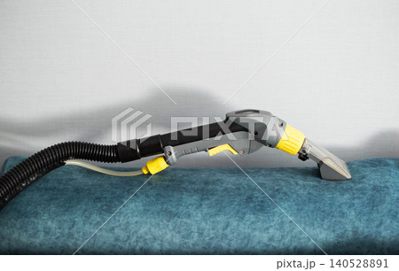 Professional deep cleaning of upholstered furniture surface using powerful wet extraction vacuum cleaner tool on blue sofa cushion Professional deep cleaning of upholstered furniture surface using powerful wet extraction vacuum cleaner tool on blue sofa cushion 140528891