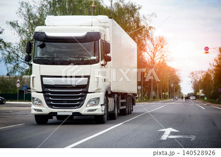 White semi-truck with cargo trailer travels on asphalt road. Long haul vehicle transportation of goods. Logistics supply chain service. 140528926