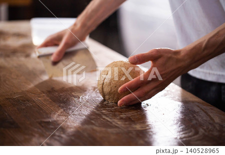 Baker hands shaping dough ball on wood surface during bread making process, preparing fresh ingredient for artisan bakery, close up detail of culinary craft 140528965