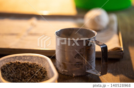 Metal flour sifter covered in white powder on wooden countertop with dough ball and plastic container of spices in soft light kitchen setting preparation for baking Metal flour sifter covered in white powder on wooden countertop with dough ball and plastic container of spices in soft light kitchen setting preparation for baking 140528968