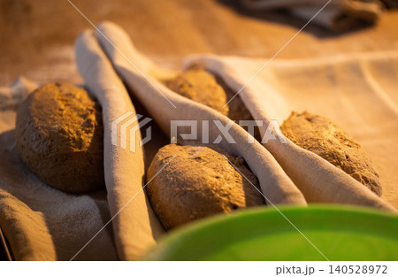 Handcrafted artisan bread dough loaves resting on floured couche fabric in warm ambient light, awaiting final proofing before baking in artisanal bakery Handcrafted artisan bread dough loaves resting on floured couche fabric in warm ambient light, awaiting final proofing before baking in artisanal bakery 140528972