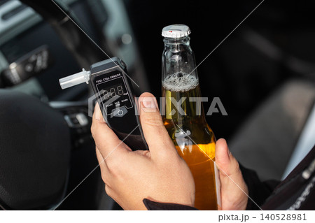 Man In Car Holding Beer Bottle And Breathalyzer. Concept Of Driving Under The Influence. Man In Car Holding Beer Bottle And Breathalyzer. Concept Of Driving Under The Influence. 140528981