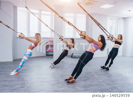 Beautiful young sports women are working out with TRX in gym Beautiful young sports women are working out with TRX in gym 140529559
