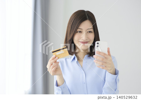 クレジットカードを持ちスマートフォンで決済をする女性 キャッシュレス社会のイメージ クレジットカードを持ちスマートフォンで決済をする女性 キャッシュレス社会のイメージ 140529632
