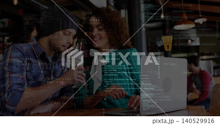 Leaning trio with beanie, plaid, teal jacket working on silver laptop at cafe showing code overlay 140529916