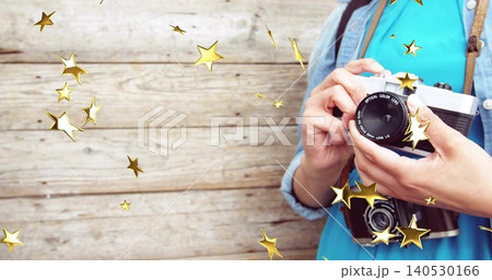 Holding SLR, lady in dress and denim-jacket posing by wood-wall with 2-cam gold stars, copy space 140530166