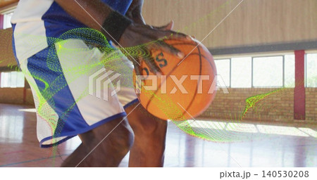 Dribbling mature player controlling orange basketball at knee height on gym court, with blue shorts 140530208