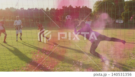 Diving goalkeeper in dark kit stretching toward soccer ball at sports field, goal net, copy space Diving goalkeeper in dark kit stretching toward soccer ball at sports field, goal net, copy space 140531356