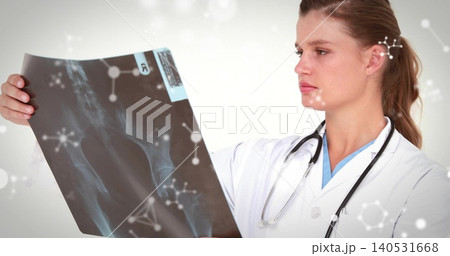 Examining clinician wearing lab coat and blue scrubs, holding pelvic X-ray, stethoscope in clinic 140531668