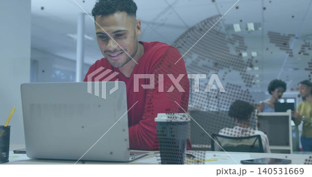 Leaning man in red long-sleeve top working on silver laptop at open-plan office, with coffee cup Leaning man in red long-sleeve top working on silver laptop at open-plan office, with coffee cup 140531669