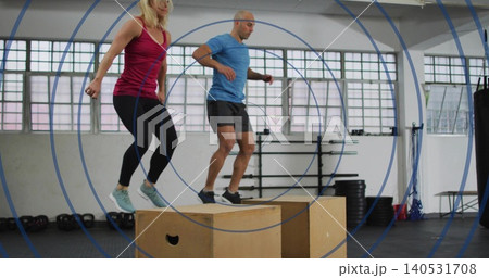 Jumping two partners landing on plyo boxes in fitness gym, wearing maroon tank and blue shirt Jumping two partners landing on plyo boxes in fitness gym, wearing maroon tank and blue shirt 140531708