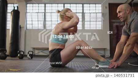 Doing sit-ups trainee wearing gear at gym, trainer holding feet with kettlebells, timestamp overlay Doing sit-ups trainee wearing gear at gym, trainer holding feet with kettlebells, timestamp overlay 140531731
