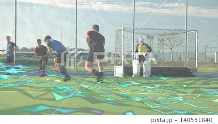 Advancing hockey players running toward ball on turf with teal overlay, keeper wearing yellow kit Advancing hockey players running toward ball on turf with teal overlay, keeper wearing yellow kit 140531840