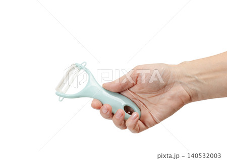 Vegetable peeler in the woman's hand on the white background. Vegetable peeler in the woman's hand on the white background. 140532003