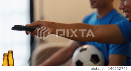 Asian man holding TV remote while watching soccer game at home Asian man holding TV remote while watching soccer game at home 140532745