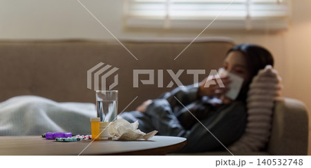 Medication and water on table with sick Asian woman in background 140532748