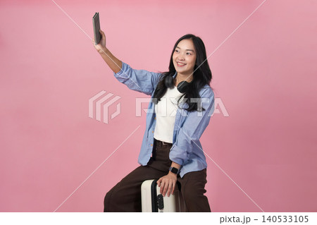 Asian woman on video call with tablet sitting on luggage for travel communication Asian woman on video call with tablet sitting on luggage for travel communication 140533105
