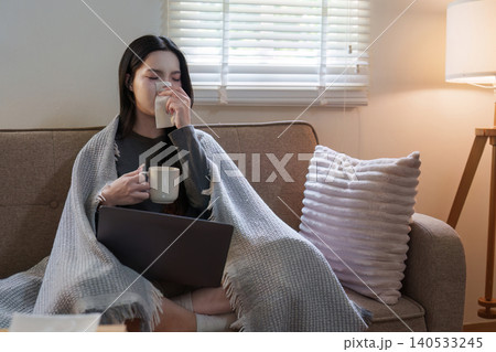 Asian woman blowing nose while working on laptop at home for remote work Asian woman blowing nose while working on laptop at home for remote work 140533245