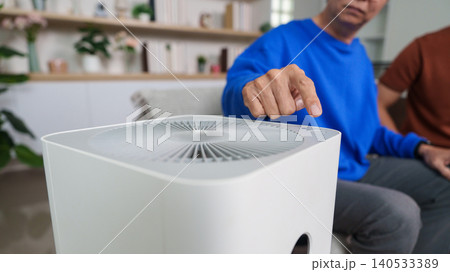 East Asian senior man adjusting air purifier in modern living room East Asian senior man adjusting air purifier in modern living room 140533389