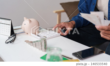 Asian man calculating savings and expenses with piggy bank at home Asian man calculating savings and expenses with piggy bank at home 140533540
