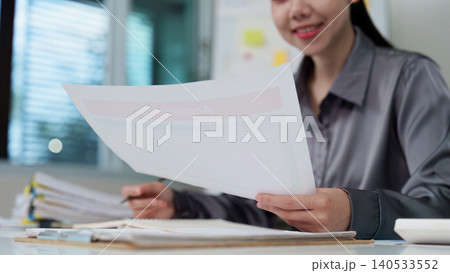 East Asian woman reviewing accounting documents in modern office East Asian woman reviewing accounting documents in modern office 140533552