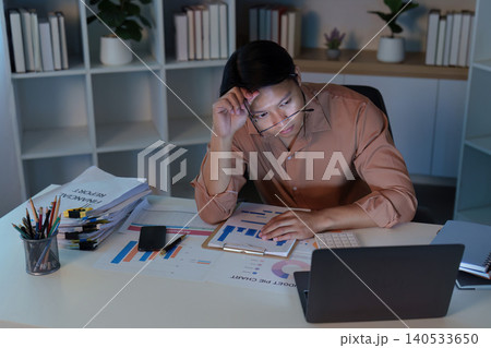 Asian man in 20s feeling stressed working late at home office 140533650
