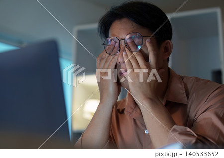 Asian man in 30s with eye strain working on laptop, fatigue Asian man in 30s with eye strain working on laptop, fatigue 140533652