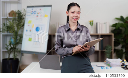 Confident Asian woman in 20s standing with clipboard at home office Confident Asian woman in 20s standing with clipboard at home office 140533790