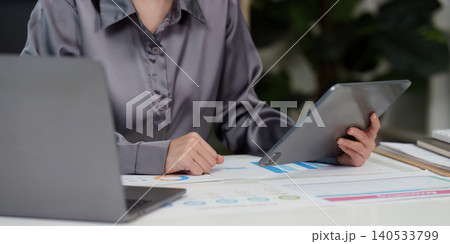 Asian woman in 20s analyzing business data on tablet and laptop Asian woman in 20s analyzing business data on tablet and laptop 140533799