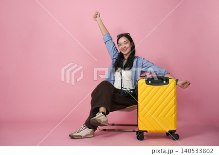 Happy Asian woman in 20s sitting on yellow suitcase, travel excitement 140533802