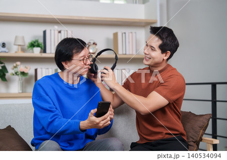 Asian son teaching senior father to use headphones and smartphone Asian son teaching senior father to use headphones and smartphone 140534094