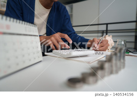 Asian man budgeting personal finance with calculator, calendar, and savings 140534156