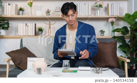 Asian man budgeting personal finance and saving money with piggy bank at home Asian man budgeting personal finance and saving money with piggy bank at home 140534158